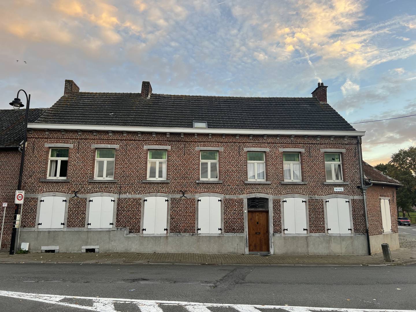 The street front of the Hof ten Berg farmhouse at sunset: brick, white shutters and a wooden door